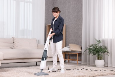 Happy young housewife vacuuming carpet at home