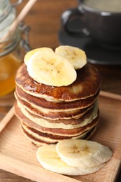 Photo of Wooden plate of banana pancakes on table, closeup