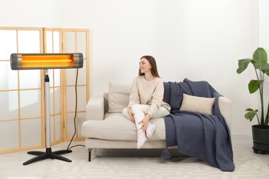 Woman warming near electric infrared heater indoors