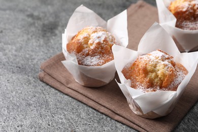 Photo of Delicious muffins with powdered sugar on grey table, closeup