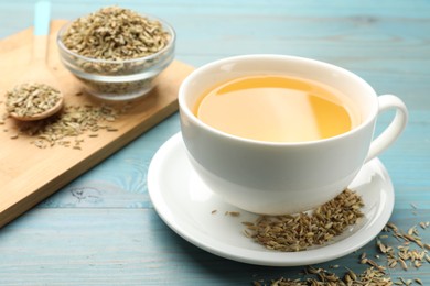 Fennel tea in cup and seeds on light blue wooden table, closeup