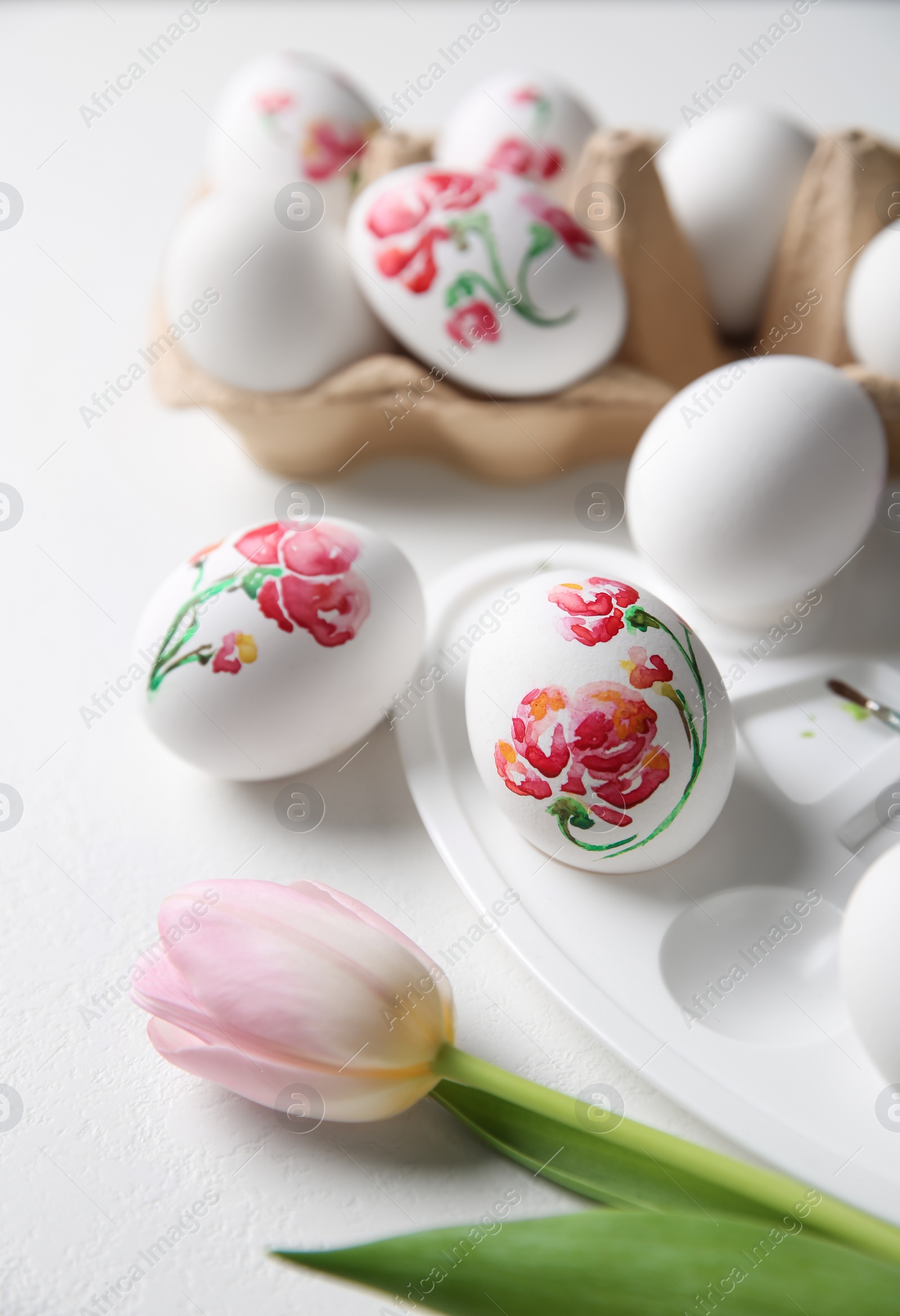 Photo of Painted Easter eggs and tulip on white table