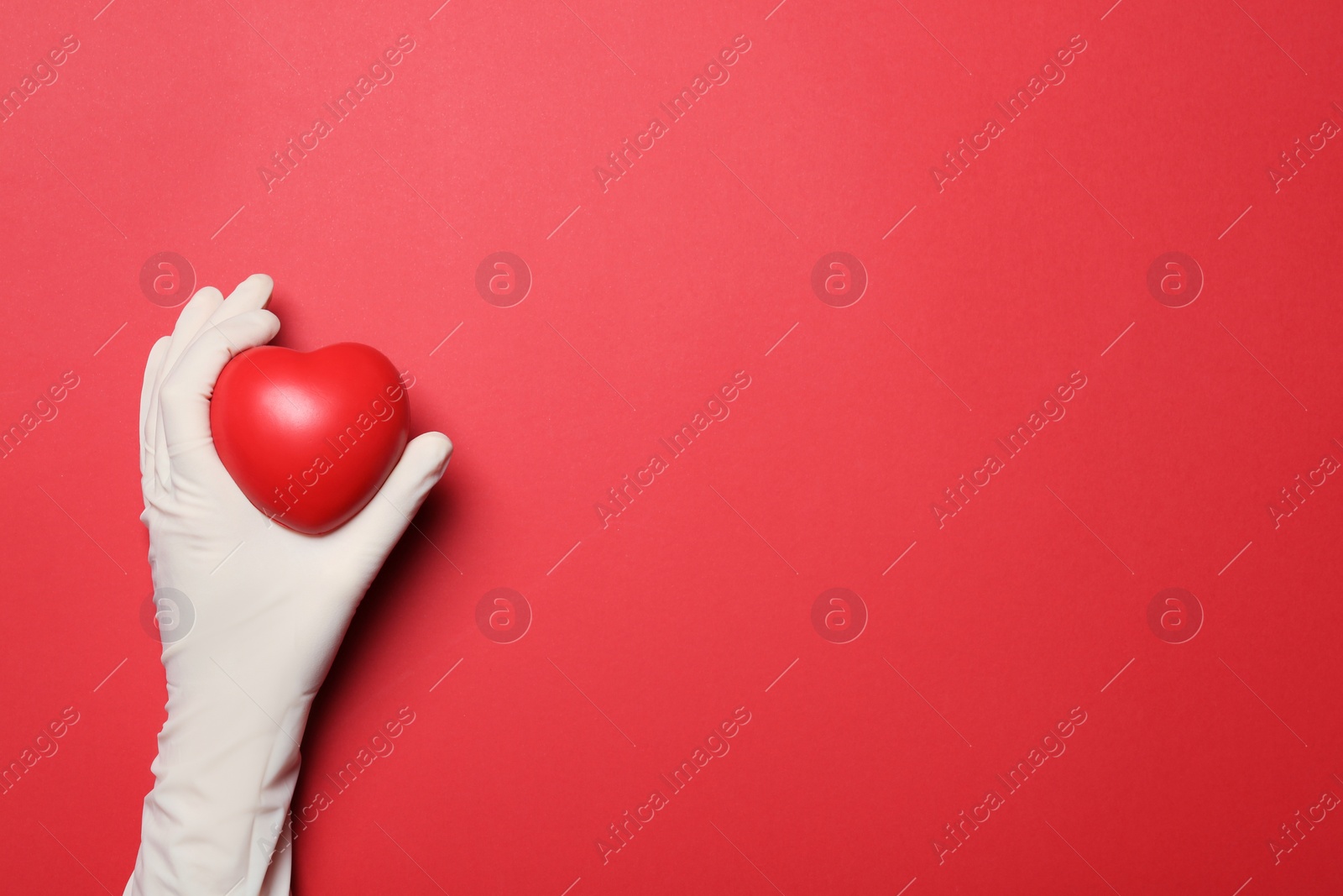 Photo of Doctor in medical glove holding heart on color background, top view. Space for text