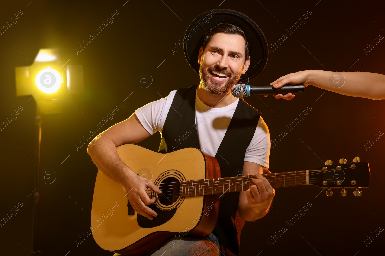 Photo of Handsome man with acoustic guitar singing while woman holding microphone on dark background, closeup