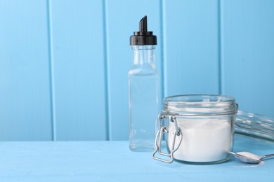 Photo of Natural cleaning products. Vinegar in bottle, baking soda and spoon on light blue wooden table. Space for text