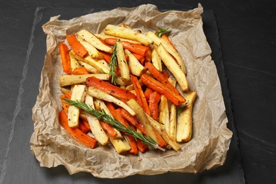 Photo of Parchment with tasty baked parsnip and bell pepper on dark grey table