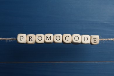 Photo of Word Promocode made of beads with letters hanging on rope against blue background
