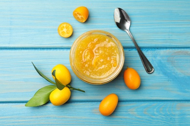 Photo of Jar of delicious kumquat jam, spoon and fresh fruits on light blue wooden table, flat lay