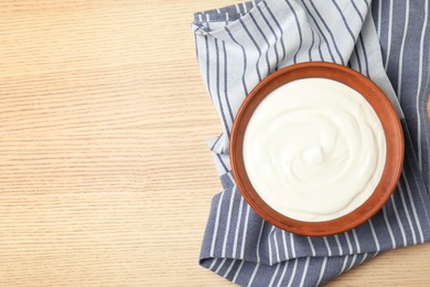 Photo of Bowl of fresh yogurt and napkin on wooden background, top view. Space for text