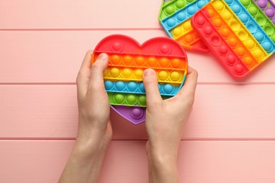 Woman using heart shaped pop it fidget toy at pink wooden table, top view