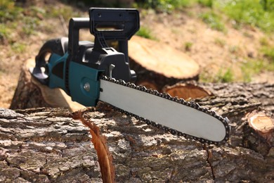 Photo of Modern electric saw and wooden log outdoors