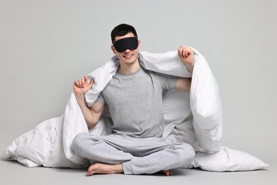 Photo of Happy man in pyjama and sleep mask wrapped in blanket on grey background