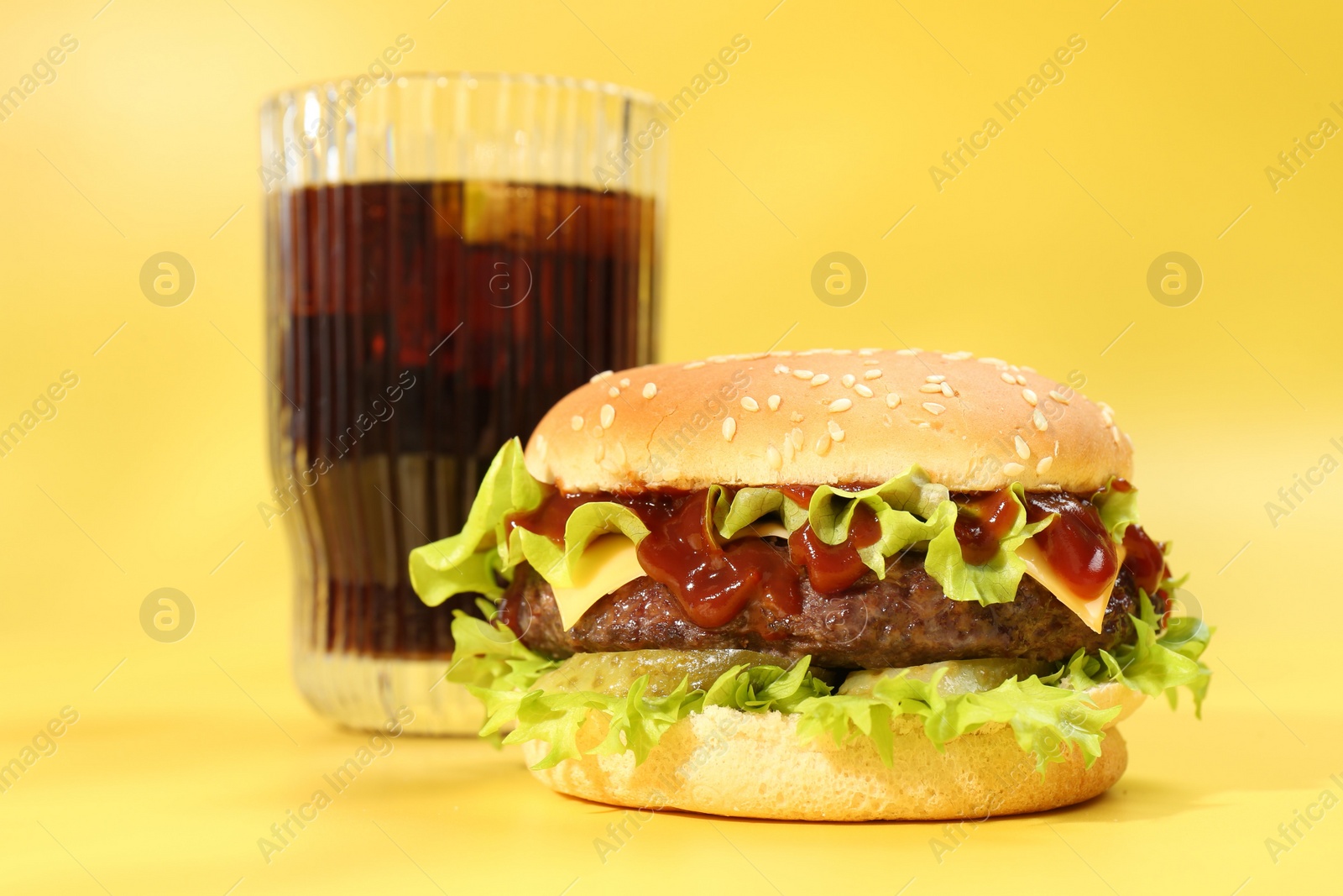 Photo of Burger with delicious patty and soda drink on yellow background, closeup