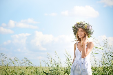 Young woman wearing wreath made of beautiful flowers in field on sunny day
