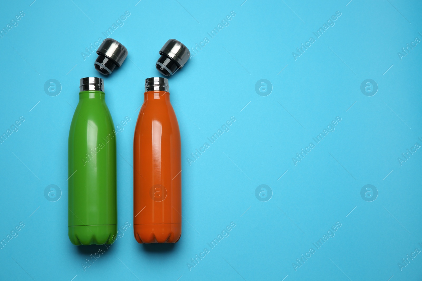 Photo of Modern thermo bottles on light blue background, flat lay. Space for text