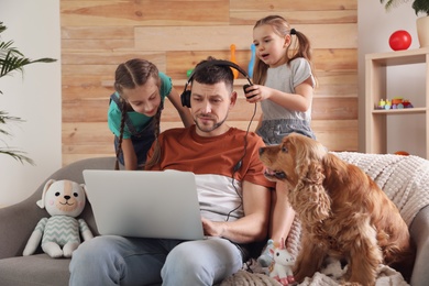 Photo of Children disturbing stressed man in living room. Working from home during quarantine