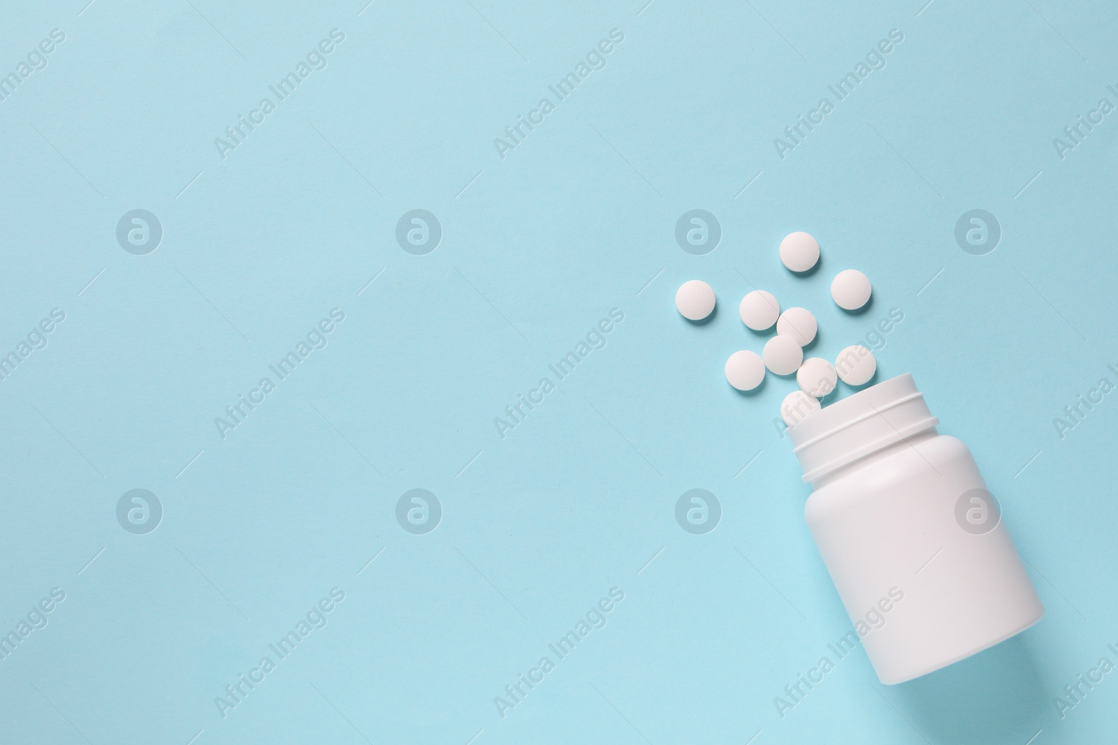 Photo of Plastic bottle with many white pills on light blue background, flat lay. Space for text