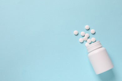 Photo of Plastic bottle with many white pills on light blue background, flat lay. Space for text