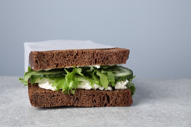 Tasty sandwich with cream cheese, cucumber and greens on light grey table