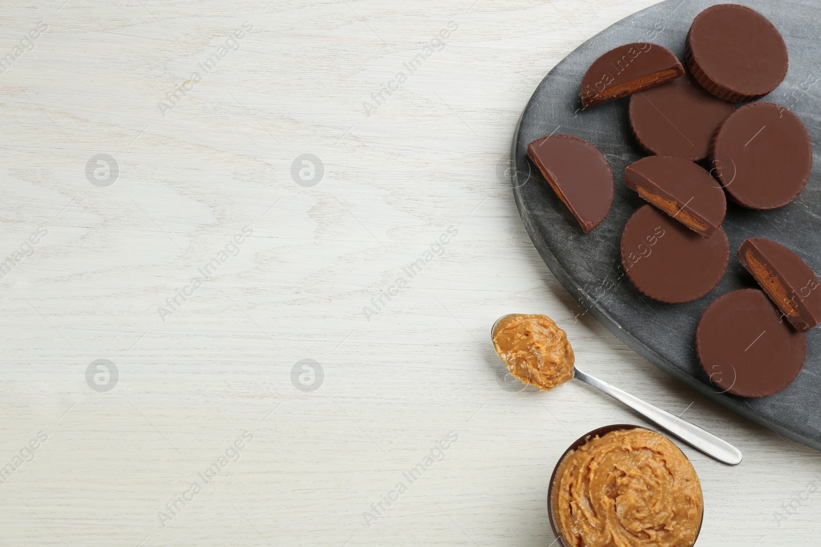 Photo of Delicious peanut butter cups on white wooden table, flat lay. Space for text