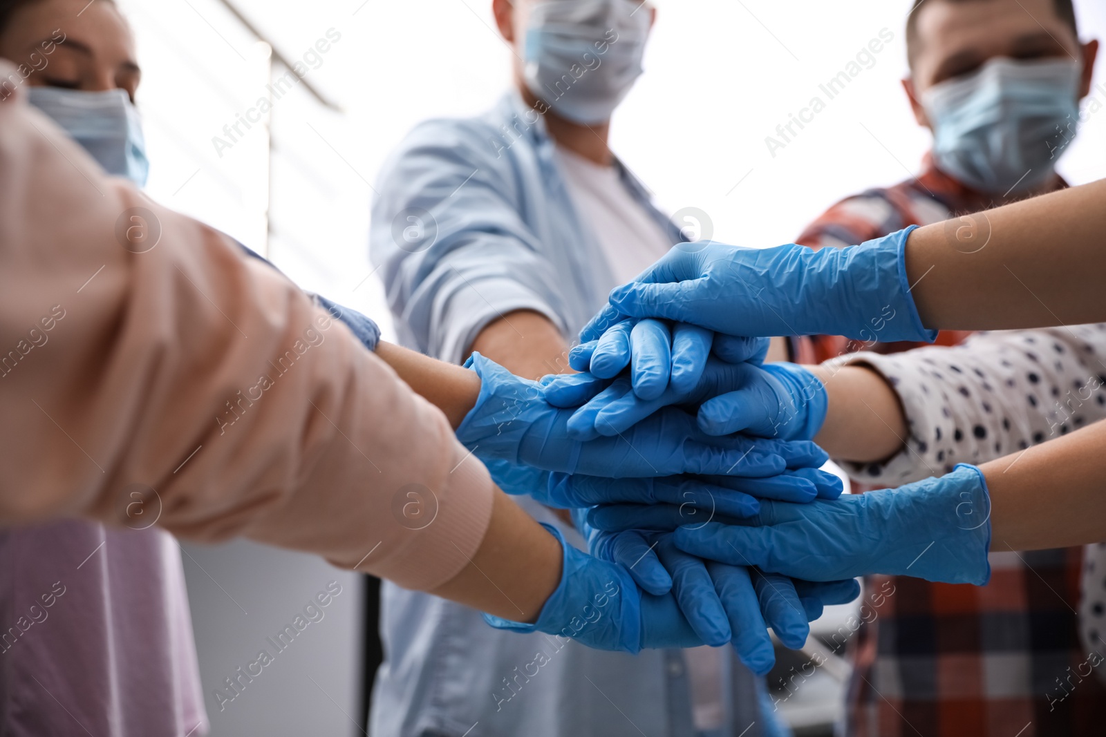 Photo of Group of people in blue medical gloves stacking hands indoors, closeup