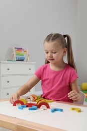 Photo of Motor skills development. Girl playing with colorful wooden arcs at white table in kindergarten