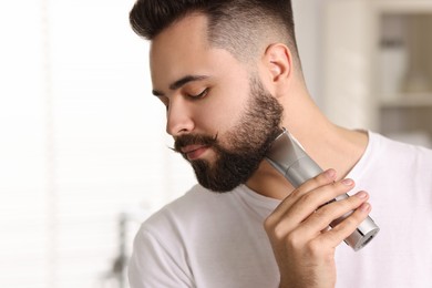 Photo of Handsome young man trimming beard at home