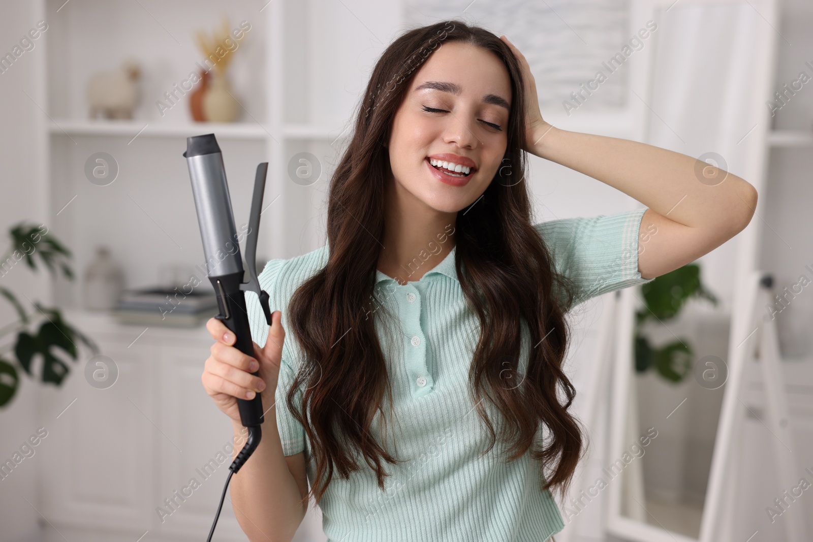 Photo of Happy woman with curling hair iron at home