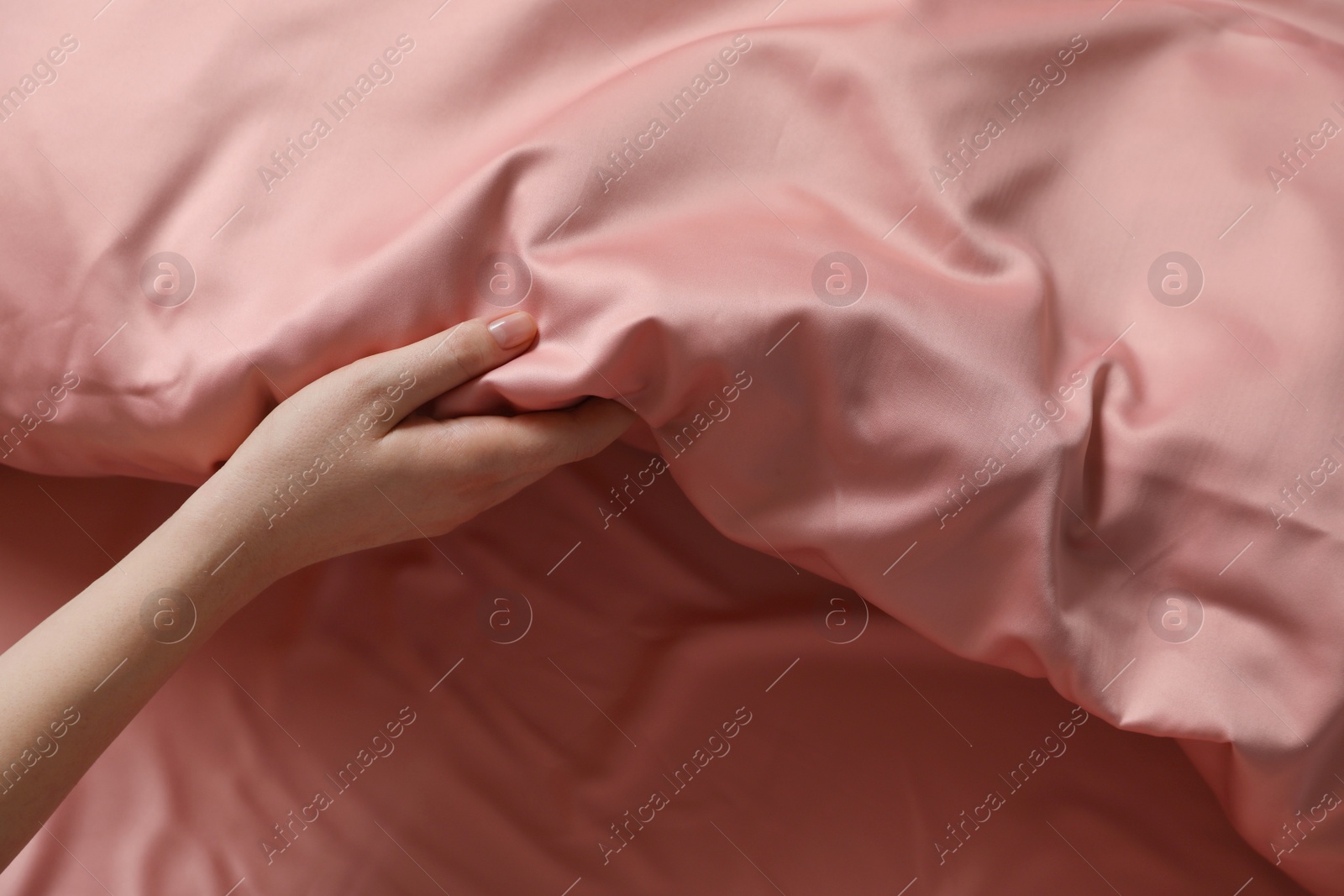 Photo of Woman making bed with beautiful pink silk linens, closeup view