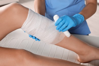 Doctor applying bandage onto patient's shin in hospital, closeup