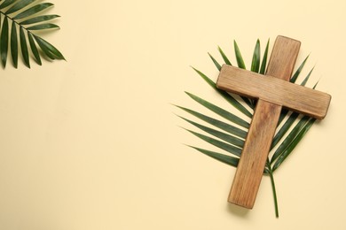 Wooden cross and palm leaves on beige background, flat lay with space for text. Easter attributes