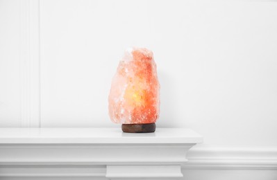 Himalayan salt lamp on console table near white wall