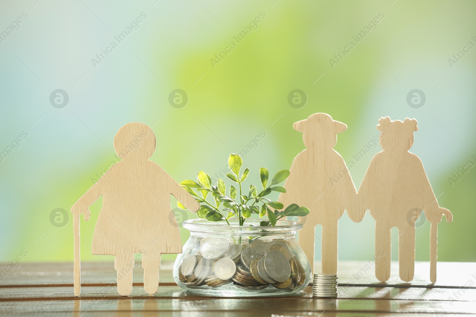 Photo of Pension savings. Figures of elderly people, coins and green twig in jar on blurred background