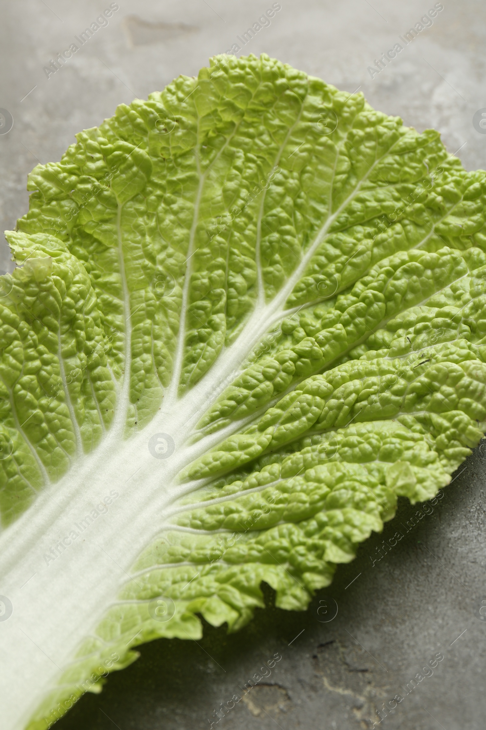 Photo of Fresh Chinese cabbage leaf on gray textured table, closeup