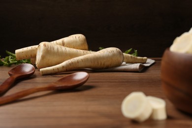 Photo of Fresh ripe parsnips and spoons on wooden table