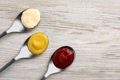 Photo of Spoons with mustard, ketchup and mayonnaise on wooden table, flat lay. Space for text
