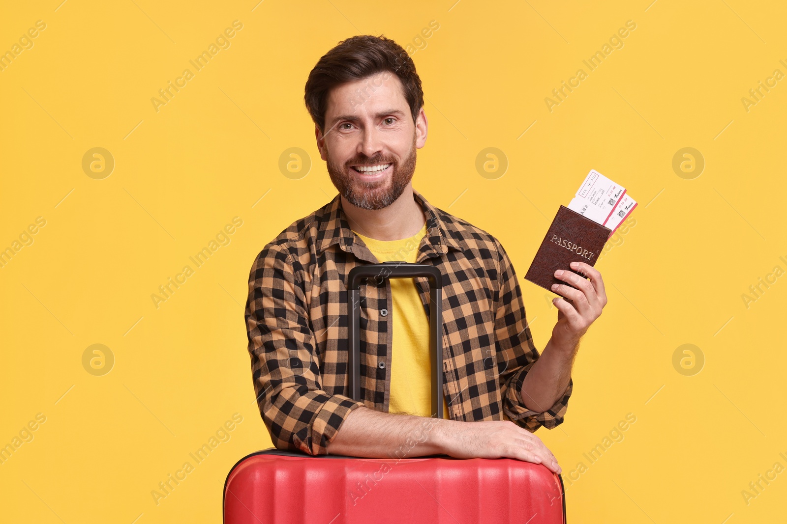 Photo of Smiling man with passport, tickets and suitcase on yellow background