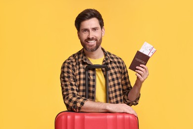 Photo of Smiling man with passport, tickets and suitcase on yellow background