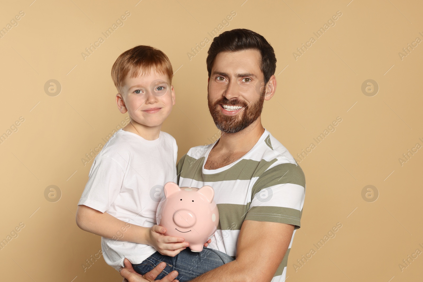Photo of Father and his son with ceramic piggy bank on beige background
