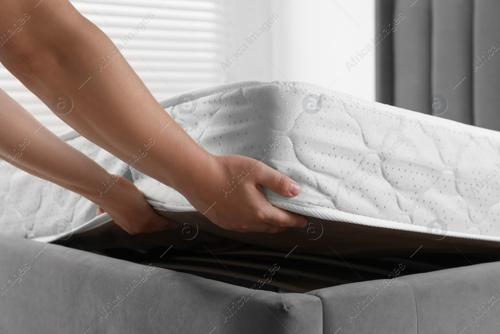 Photo of Woman putting soft light green mattress on gray bed indoors, closeup