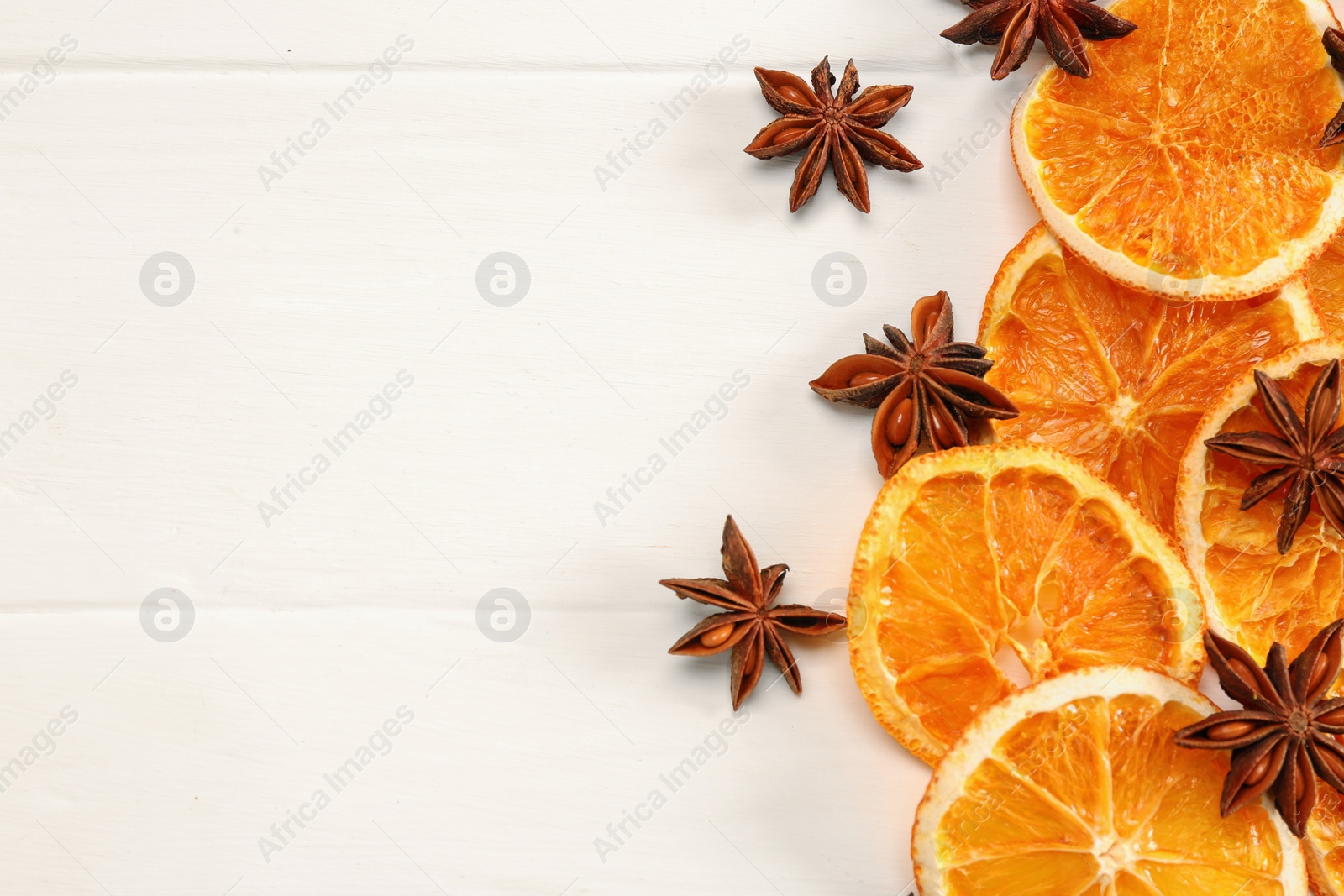 Photo of Dry orange slices and anise stars on white wooden table, flat lay. Space for text