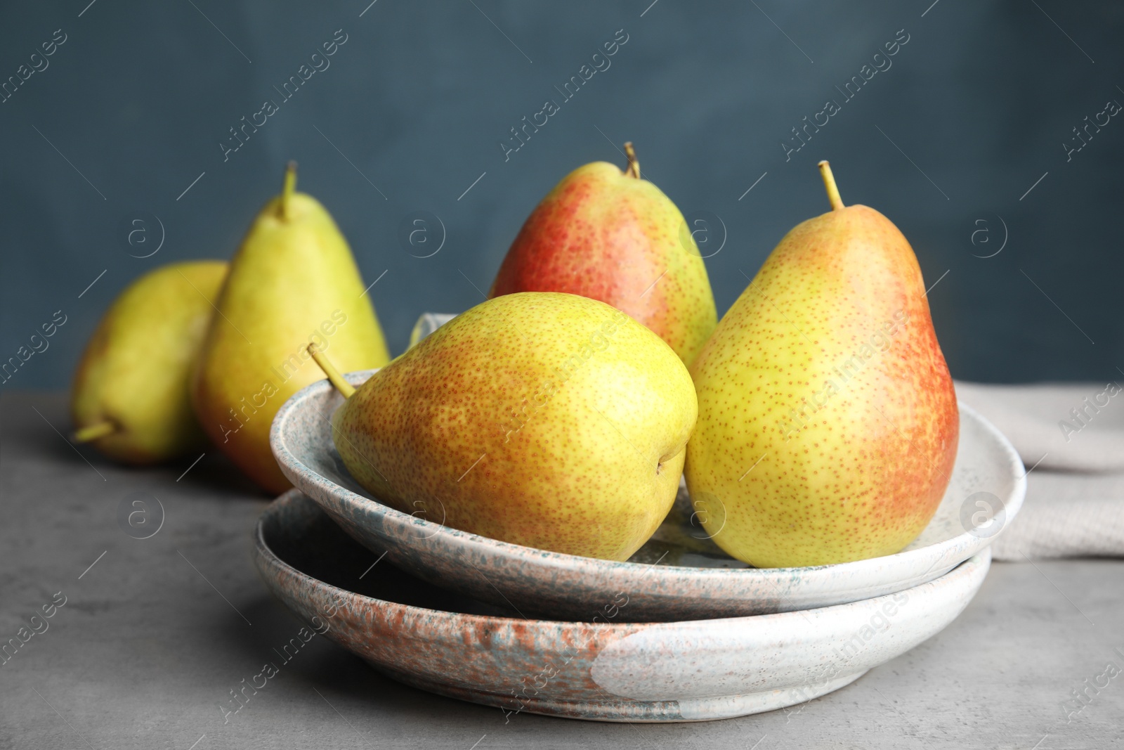 Photo of Plates with ripe juicy pears on grey stone table against blue background