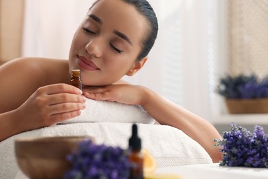 Photo of Beautiful young woman with bottle of essential oil on massage couch in spa salon