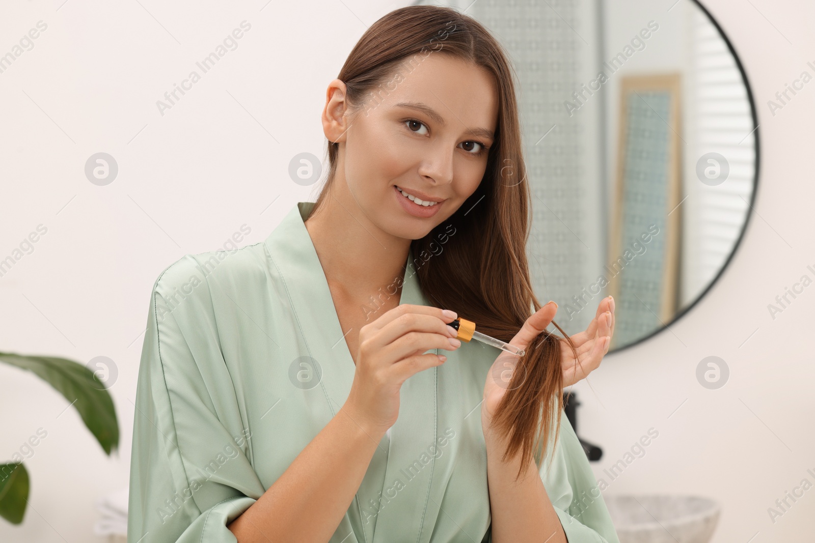 Photo of Beautiful woman applying serum onto hair indoors