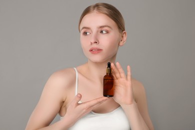 Beautiful young woman with bottle of essential oil on light grey background