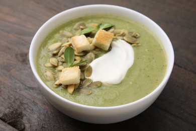 Photo of Delicious broccoli cream soup with croutons, sour cream and pumpkin seeds on wooden table, closeup
