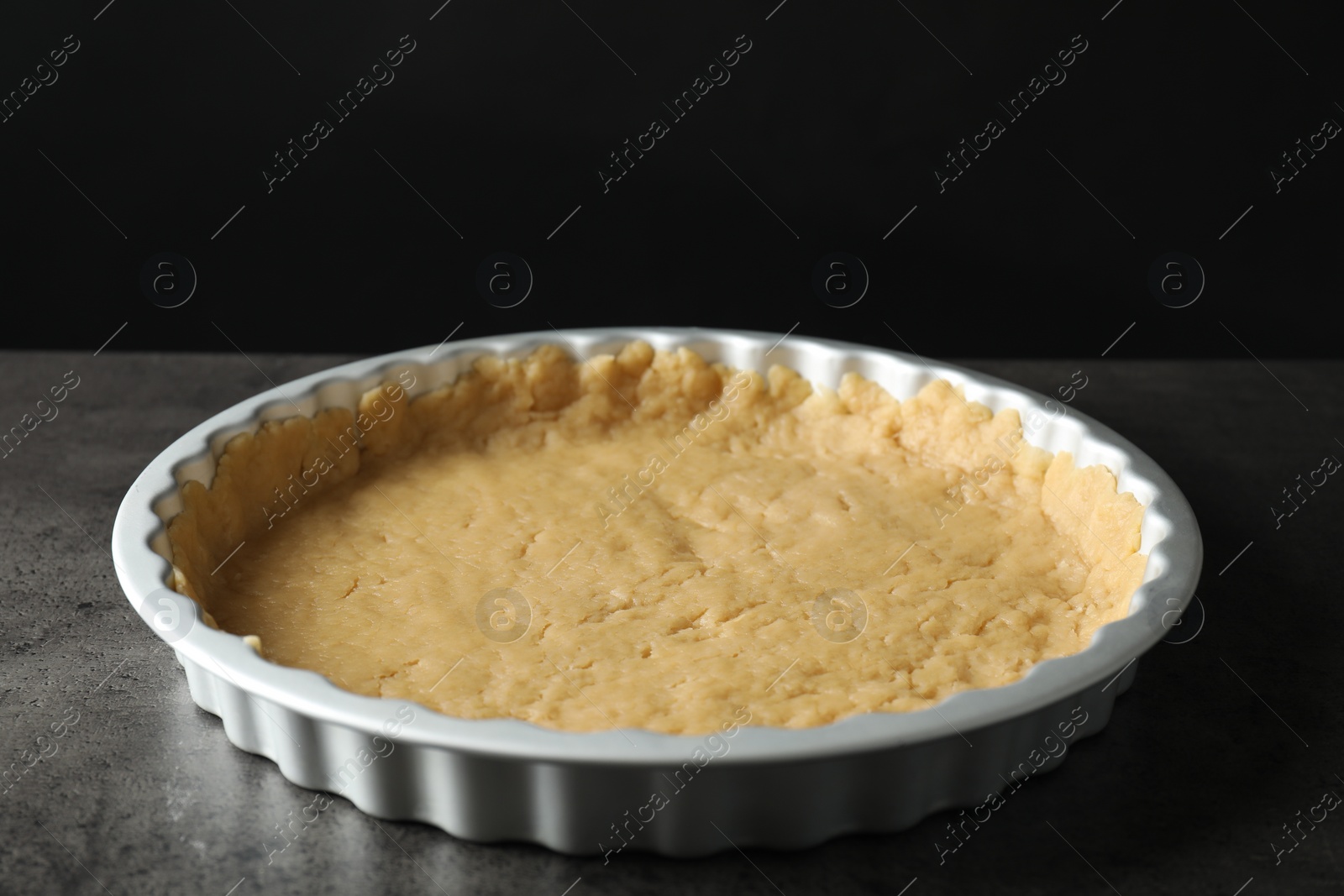 Photo of Making shortcrust pastry. Raw dough in baking dish on grey table