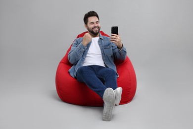 Happy young man using smartphone on bean bag chair against grey background