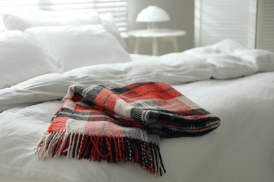 Folded warm checkered plaid on bed indoors