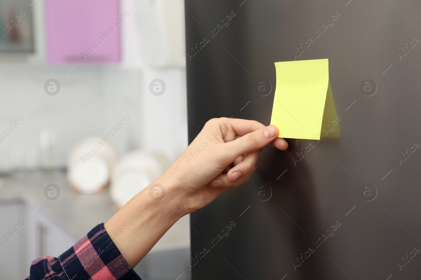 Photo of Woman putting blank sticky note on refrigerator door indoors, closeup